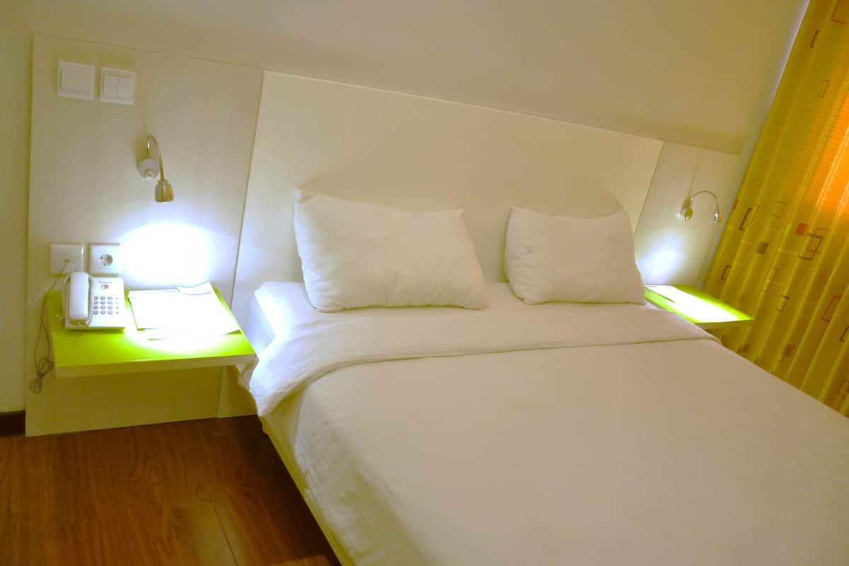 A hotel room with a large bed, two bedside tables, a telephone, and a wall-mounted light.