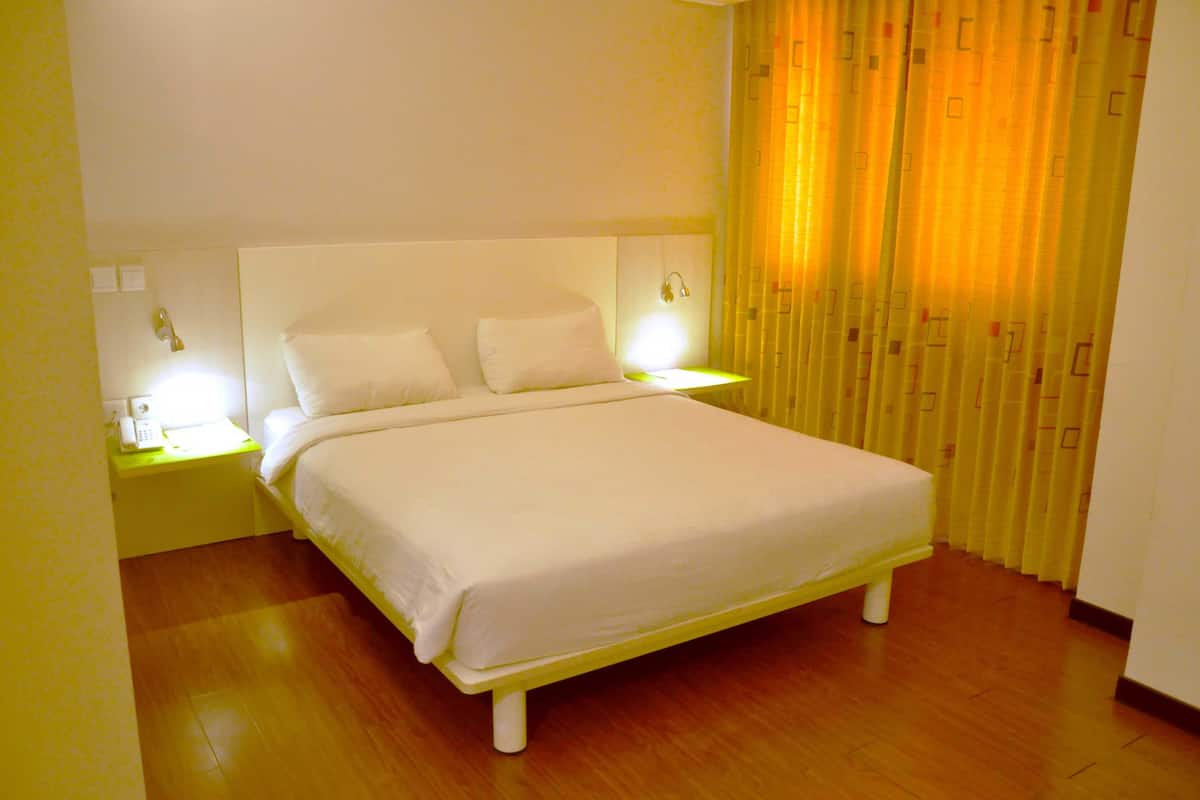 A neatly made bed with white bedding, two bedside lamps, and a telephone on a yellow bedside table.