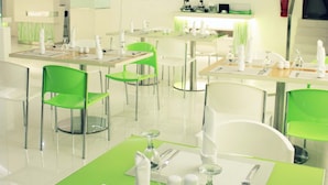 Un espace repas moderne avec des chaises vertes et des tables blanches, équipé de couverts et de serviettes.