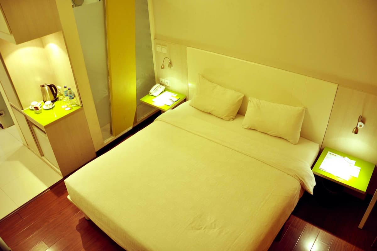 A hotel room with a large bed, a bedside table with a lamp, and a small table with a kettle and cups.