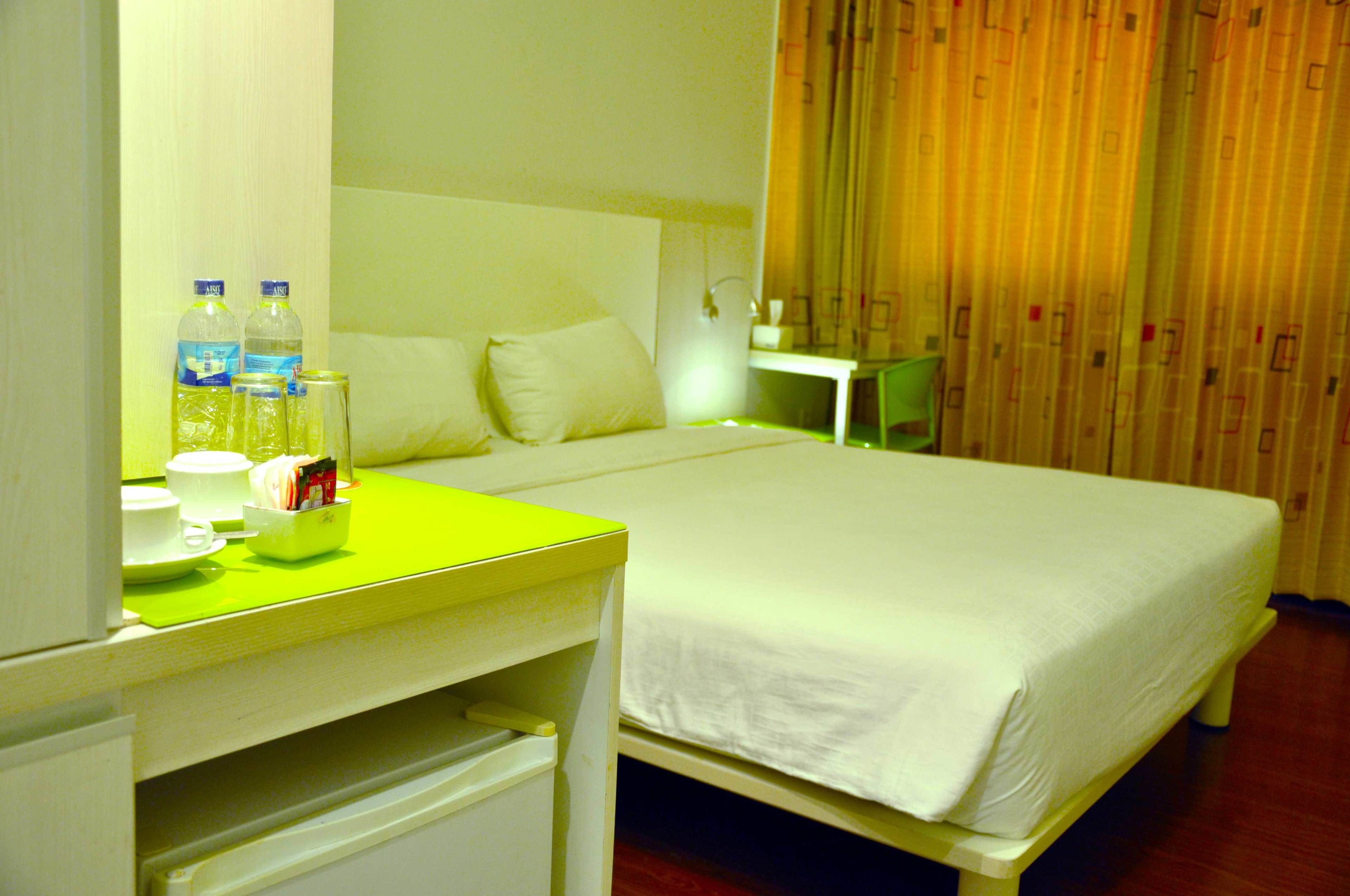 A hotel room with a bed, a desk with a chair, a nightstand, and a mirror.