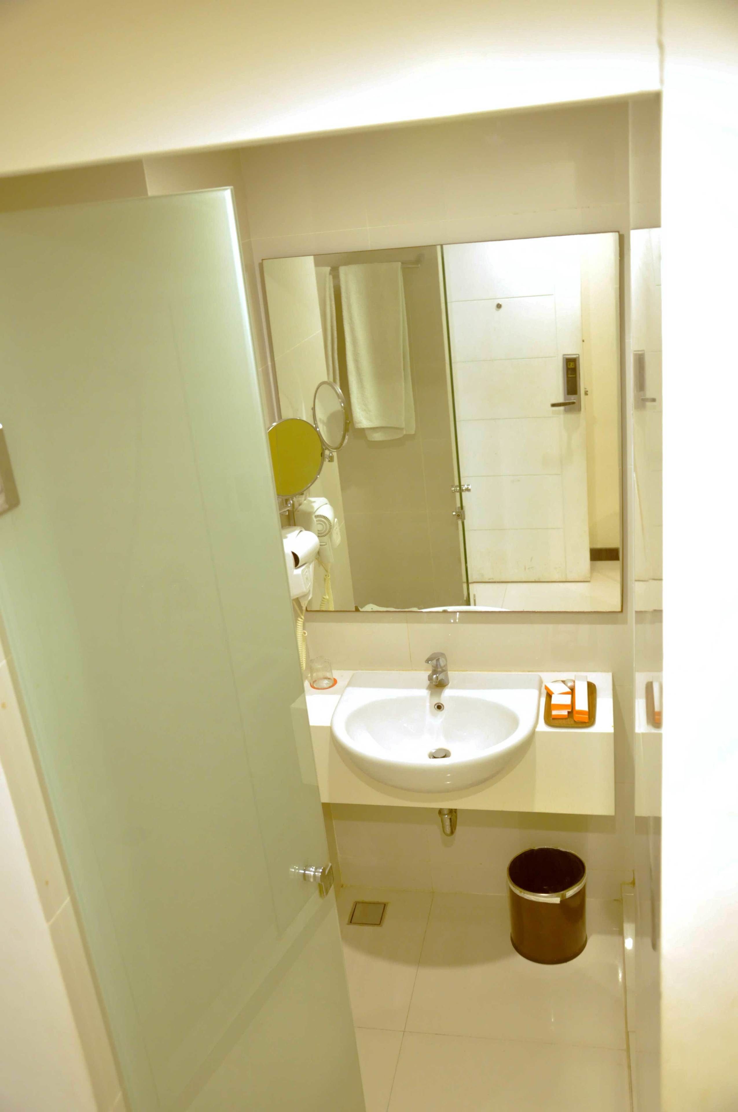 A bathroom with a white sink, a mirror, a towel dispenser, and a trash can.