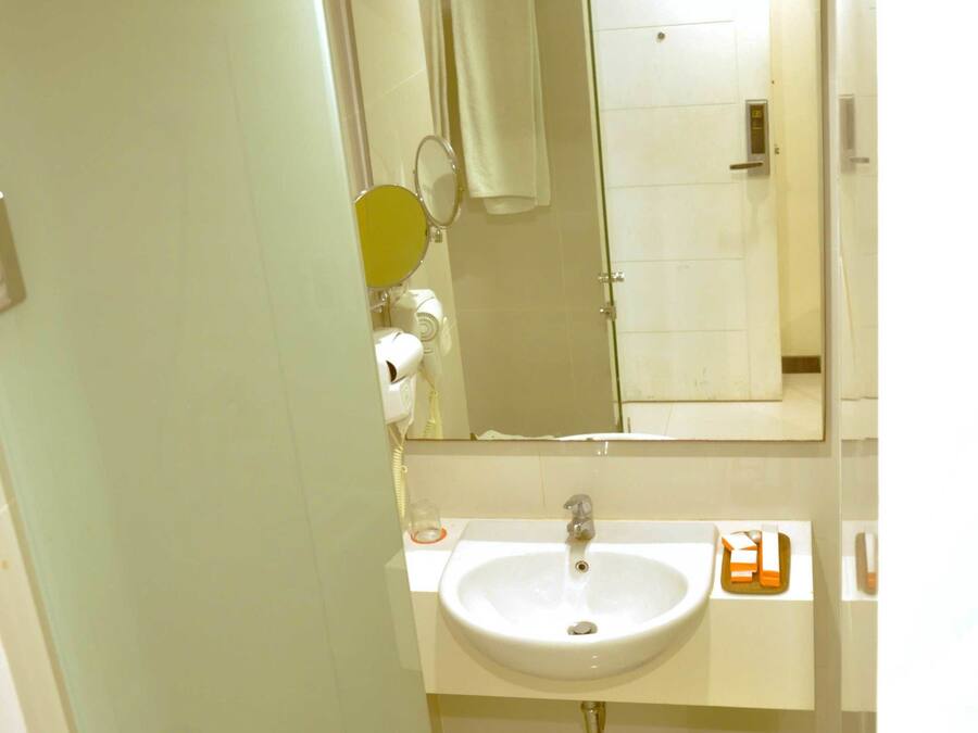 A bathroom with a white sink, a mirror, a towel dispenser, and a trash can.