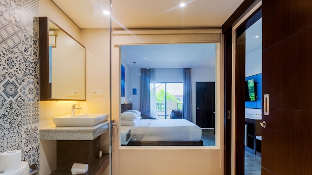 Ein modernes Hotelzimmer mit einem großen Bett, einem Badezimmer mit Waschbecken und Spiegel sowie Blick nach außen.