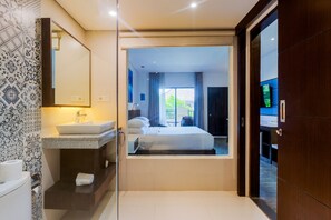 A modern hotel room with a large bed, a bathroom with a sink and mirror, and a view of the outside. - Kuta Beach Club Hotel (Kuta)