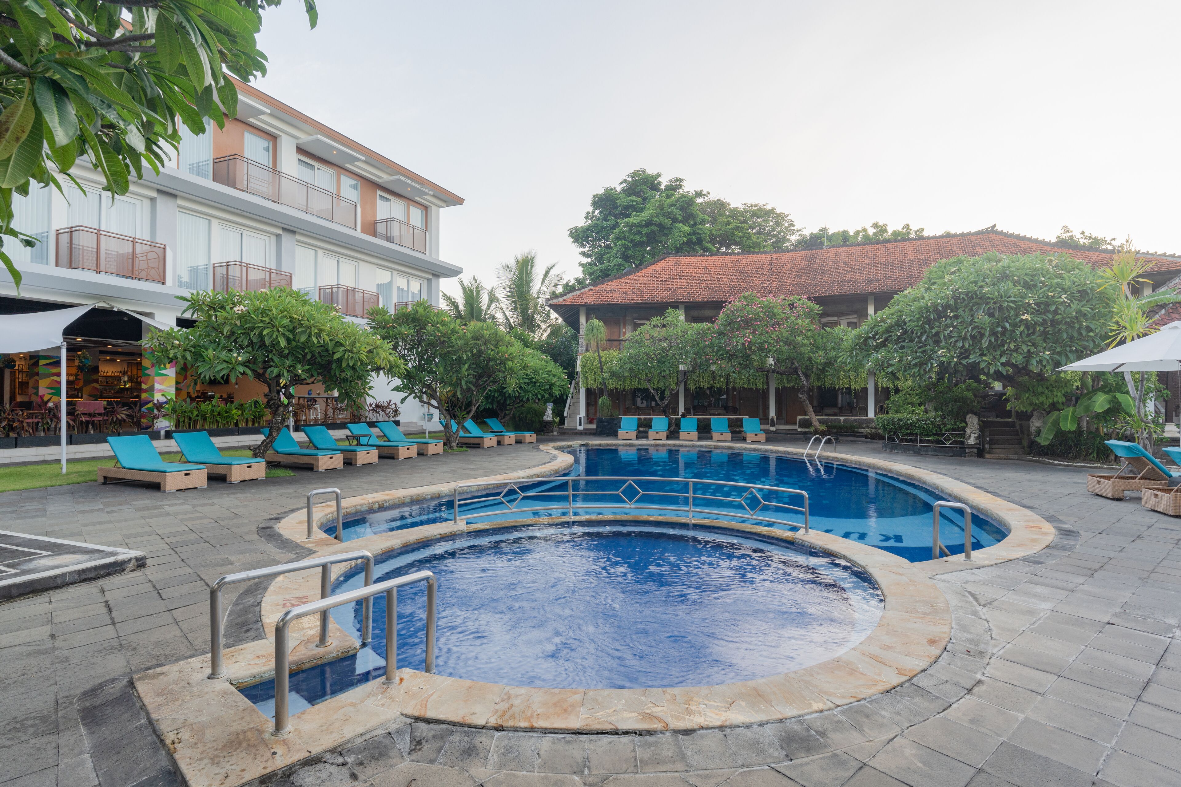 A swimming pool with a circular design, surrounded by lounge chairs and a building with balconies.