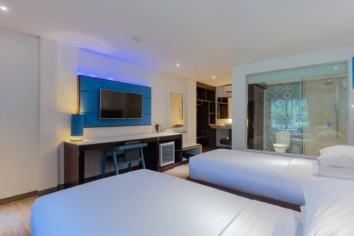 Une chambre d’hôtel moderne équipée de deux lits, d’un bureau avec une chaise, d’une télévision à écran plat et d’un dressing.