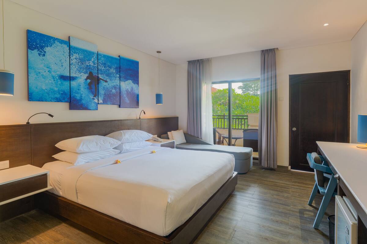 Une chambre d’hôtel moderne dotée d’un grand lit, d’un bureau et d’un balcon offrant une vue sur la verdure.