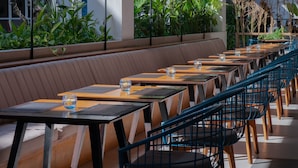 Ein modernes Restaurant mit langen Gemeinschaftstischen und gemütlichen Sitzgruppen, umgeben von viel Grün und großen Fenstern.