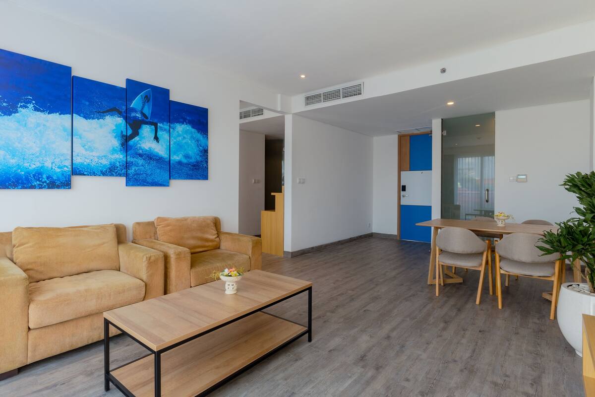 Un espace de vie moderne comprenant un canapé, une table basse et une table à manger avec des chaises. Un grand tableau orne le mur, et une plante en pot est également présente.