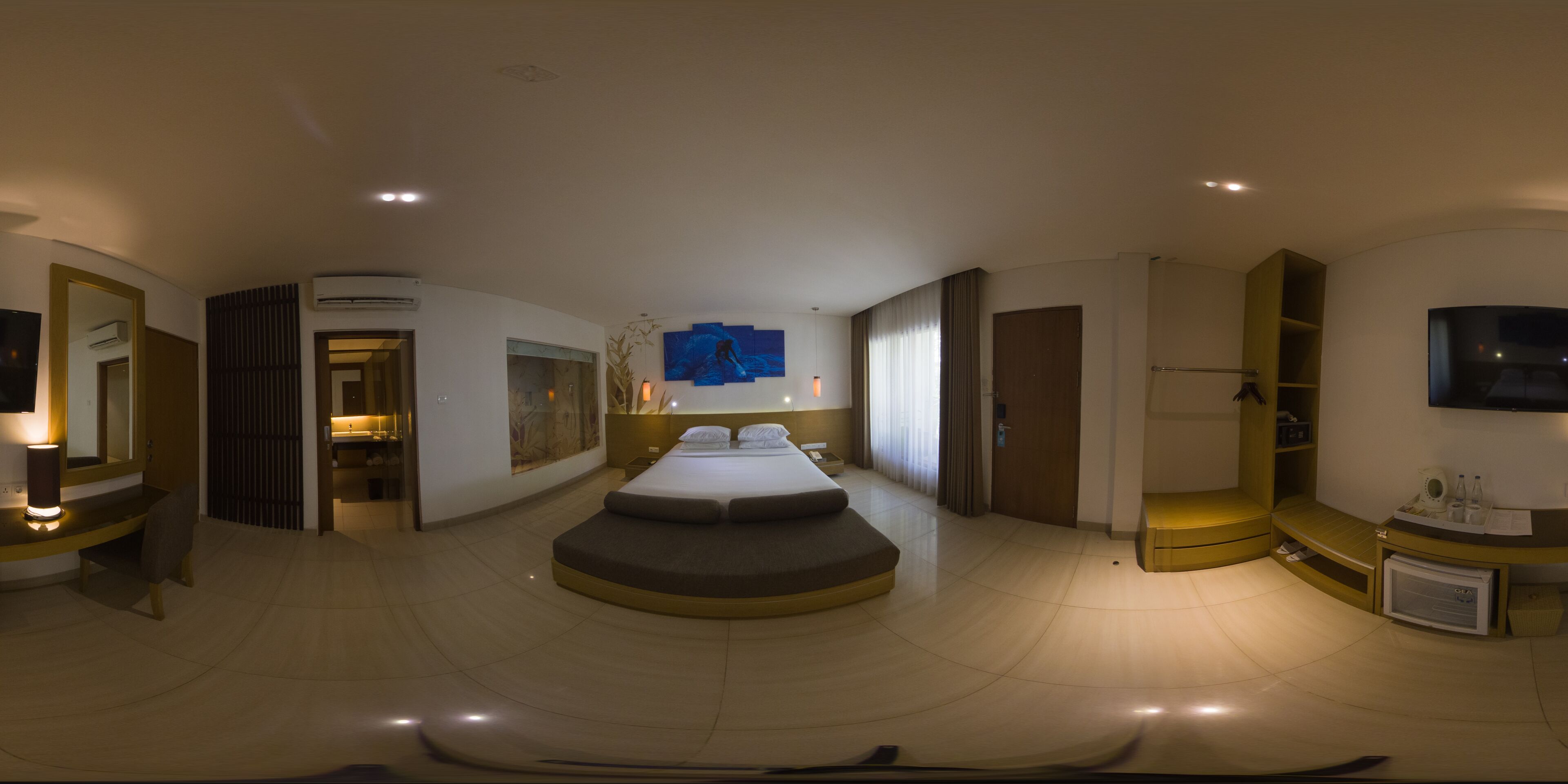 A modern hotel room with a large bed, a flat-screen TV, a desk with a lamp, and a small refrigerator.