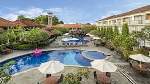 Ein Hotelpoolbereich mit Liegestühlen, Sonnenschirmen und einer kleinen Fontäne.