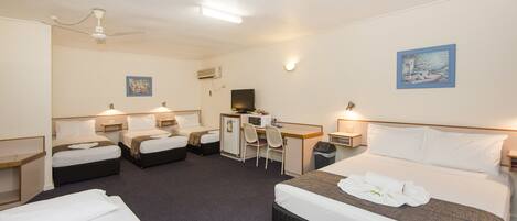 A hotel room with four beds, a desk, a chair, a television, and a small trash bin.