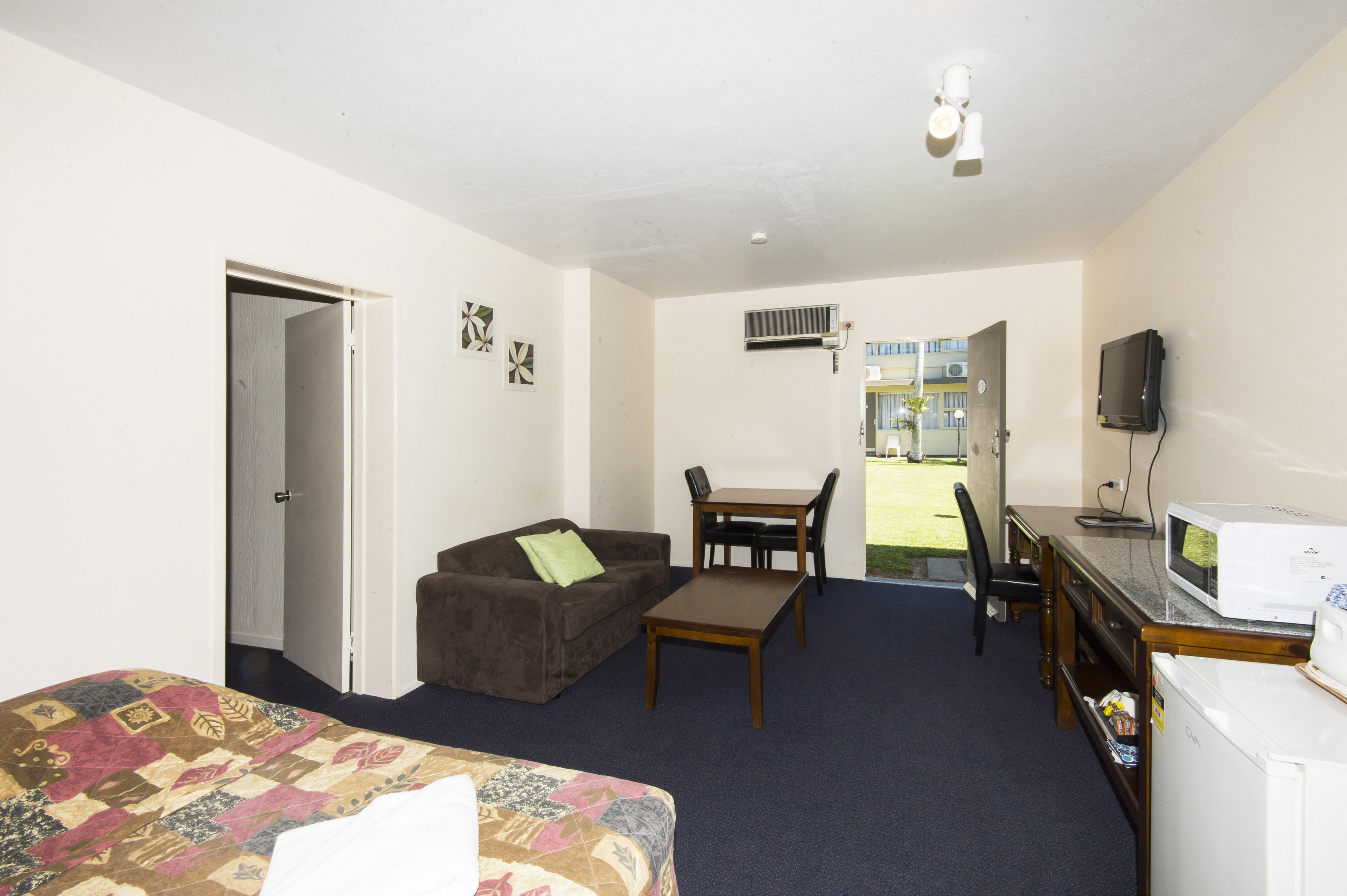 A hotel room with a bed, a brown sofa, a small table, a desk with a computer and a TV, and a microwave.