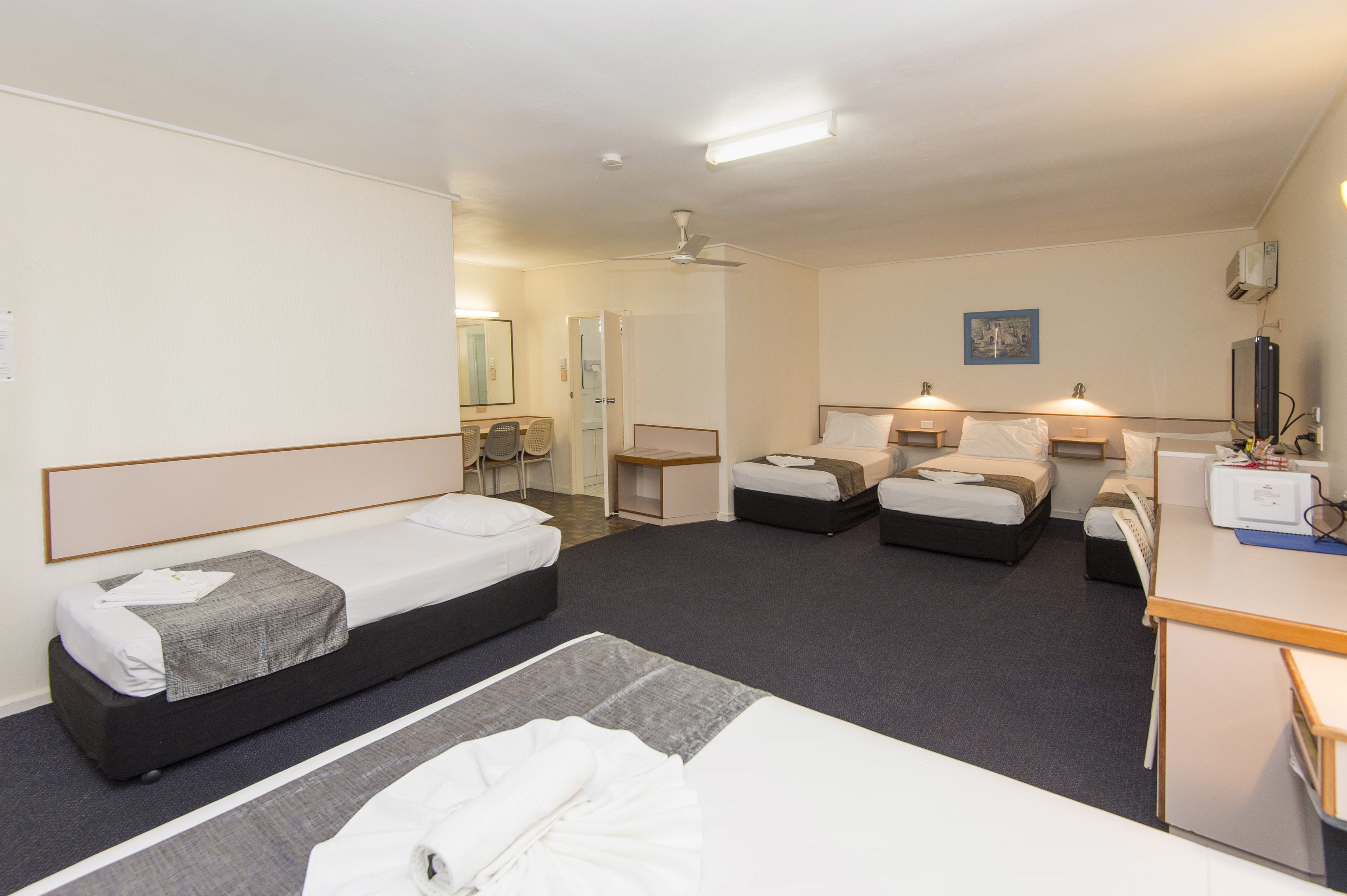 A hotel room with two single beds, a desk, a chair, and a small table.