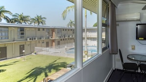 A balcony with a view of a swimming pool and palm trees, a small table with chairs, and a mounted TV.