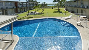 A swimming pool with a tiled deck, surrounded by lounge chairs and a fenced lawn area.