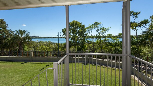 A covered outdoor area with a metal railing, a grassy lawn, and a view of a body of water and trees.