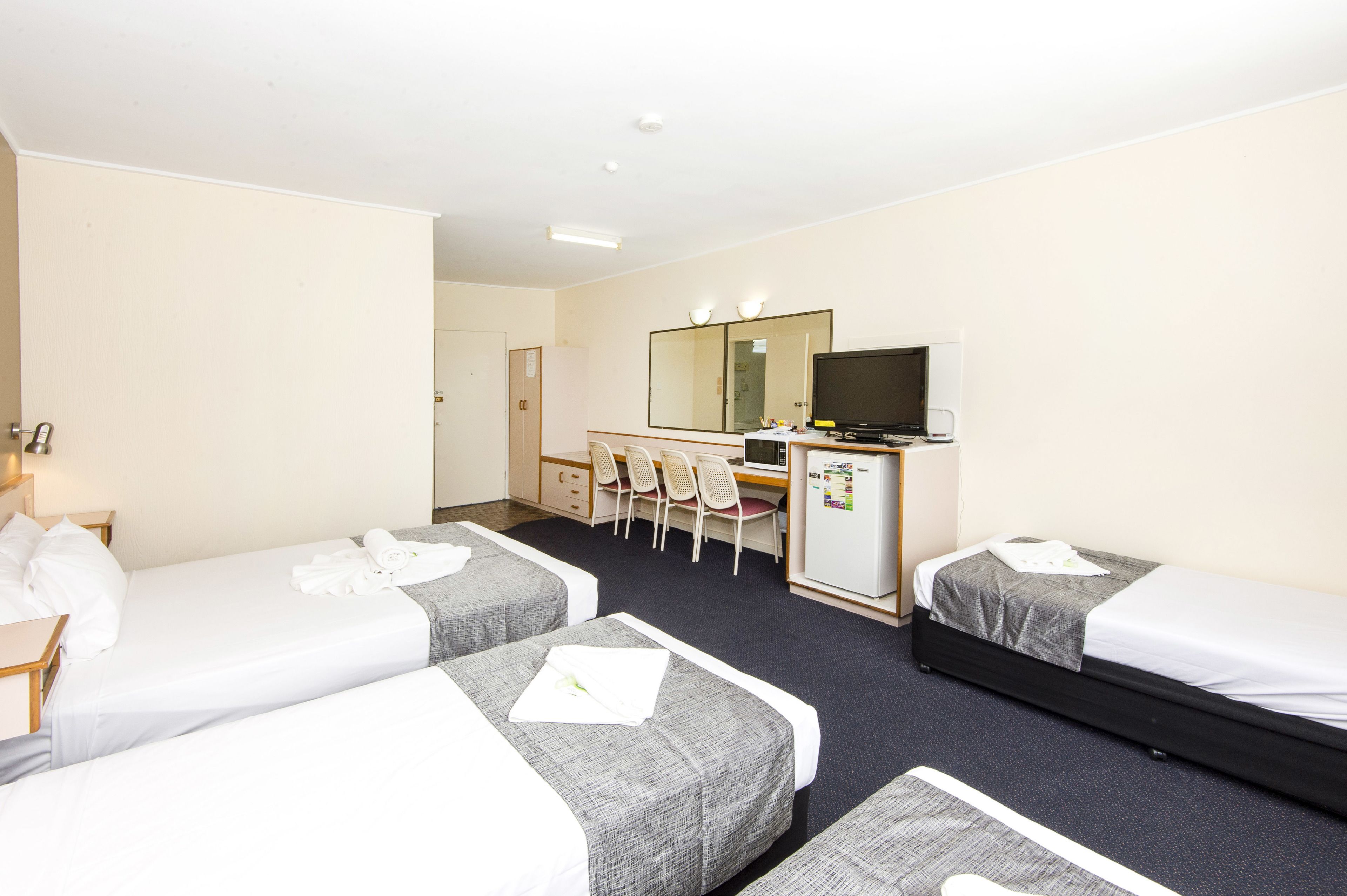A hotel room with two single beds, a desk with a computer and a TV, a mirror, and a refrigerator.