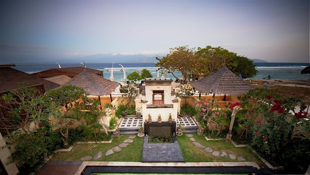 A pool area with a view of the sea, surrounded by a garden with potted plants and a small structure with a tiled roof. - Kokomo Resort Gili Trawangan (Gili Trawangan)