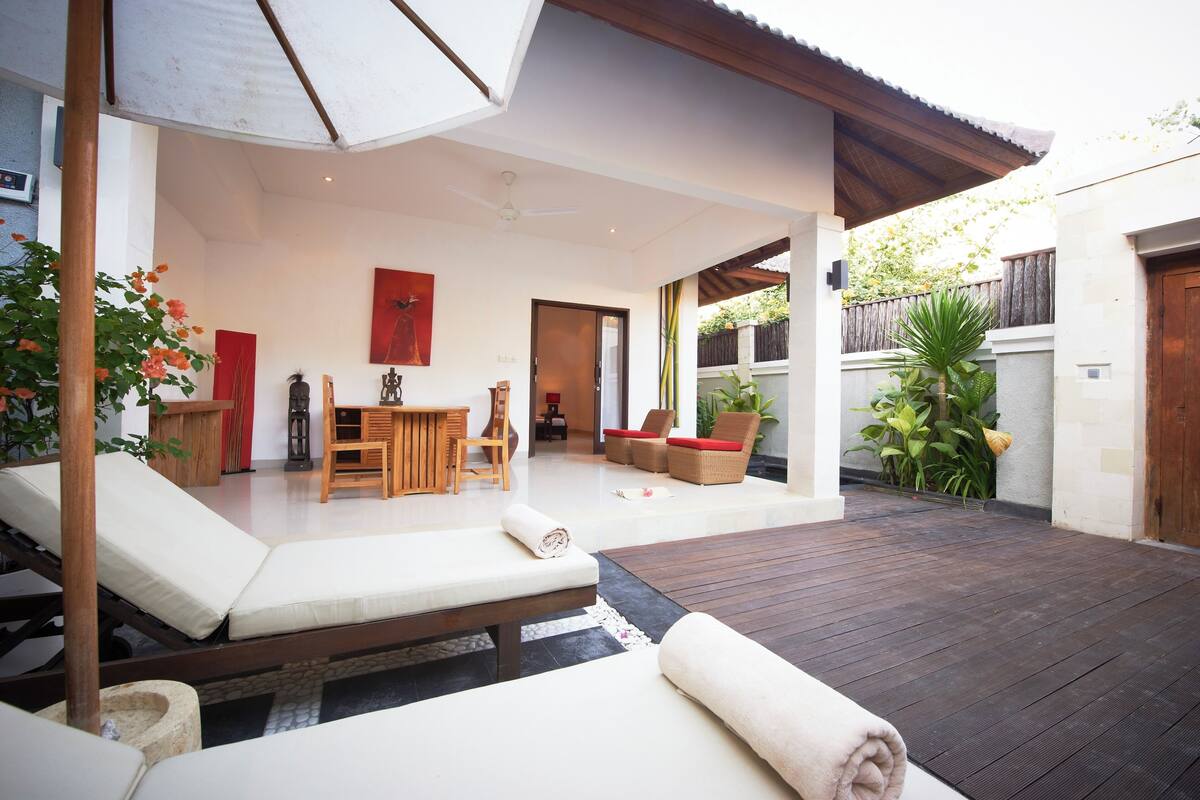 Un espacio al aire libre moderno con terraza de madera, sillones de descanso, una mesa de comedor y un ventilador de techo.