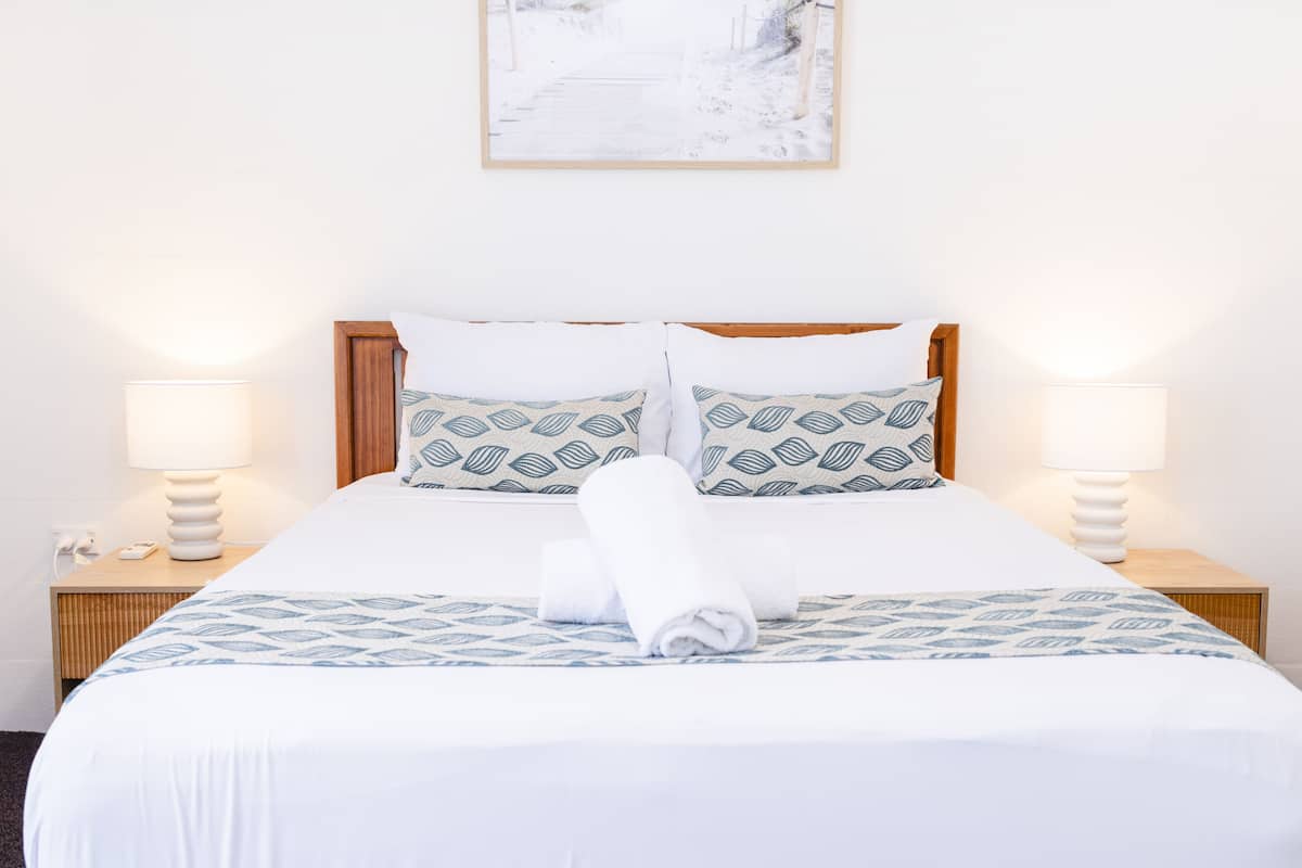 A neatly made bed with patterned pillows, a rolled towel, and two bedside lamps on wooden nightstands.