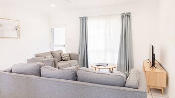 En moderne stue med en grå sofa, et træsofabord og et fjernsyn på et træstel.