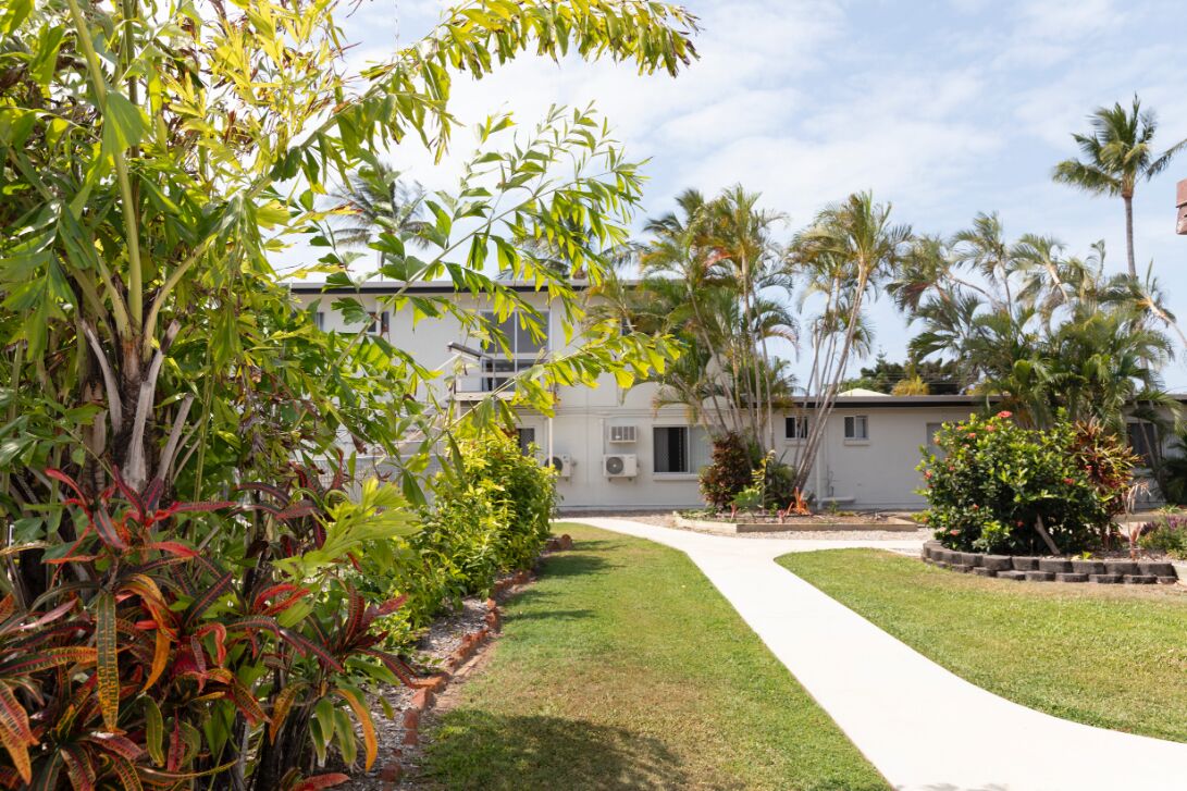 A residential building with a well-maintained lawn, a pathway leading to the entrance, and tropical vegetation around.