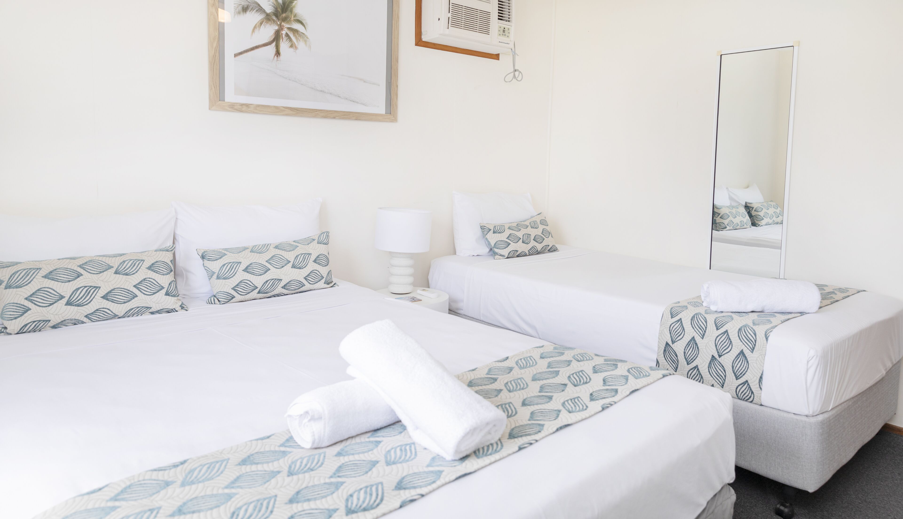 A hotel room with two beds, each with a patterned bedspread, a bedside lamp, and a mirror on the wall.