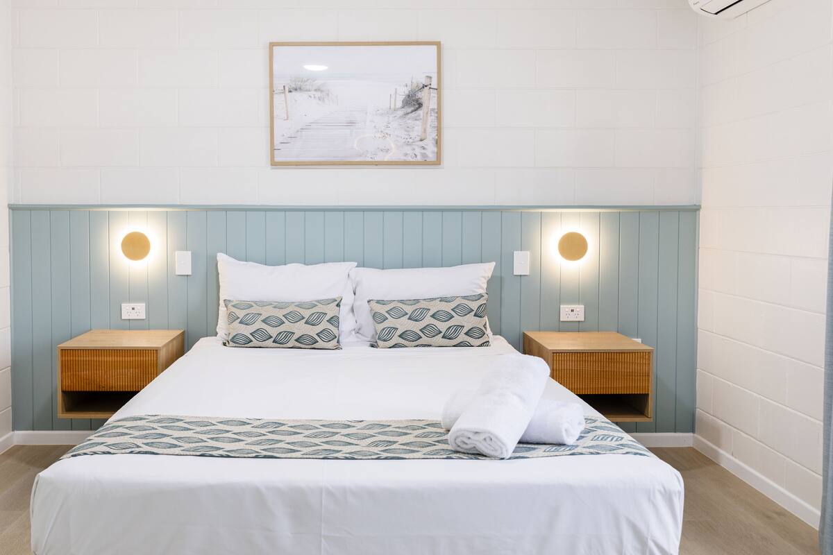 A neatly arranged bedroom with a bed, two bedside tables, and a wall-mounted light fixture.