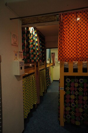 A narrow hallway with bunk beds and colorful curtains. - Hostel BASE POINT Osaka (Osaka)