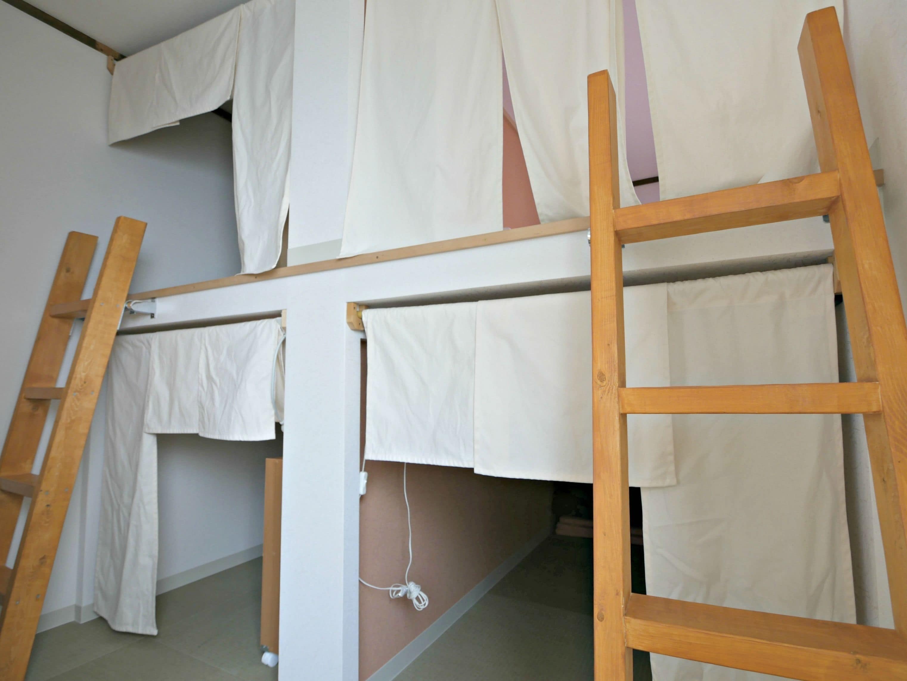 Uma cama beliche com escadas de madeira e lençóis brancos.