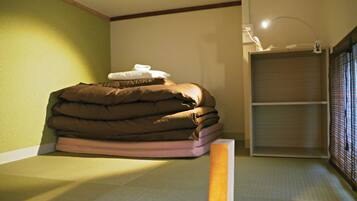 Una cama bien tendida con una pila de mantas y almohadas, una mesita de noche y una estantería contra la pared.