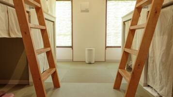 A room with two wooden bunk beds, a white air conditioner, and a small trash bin.