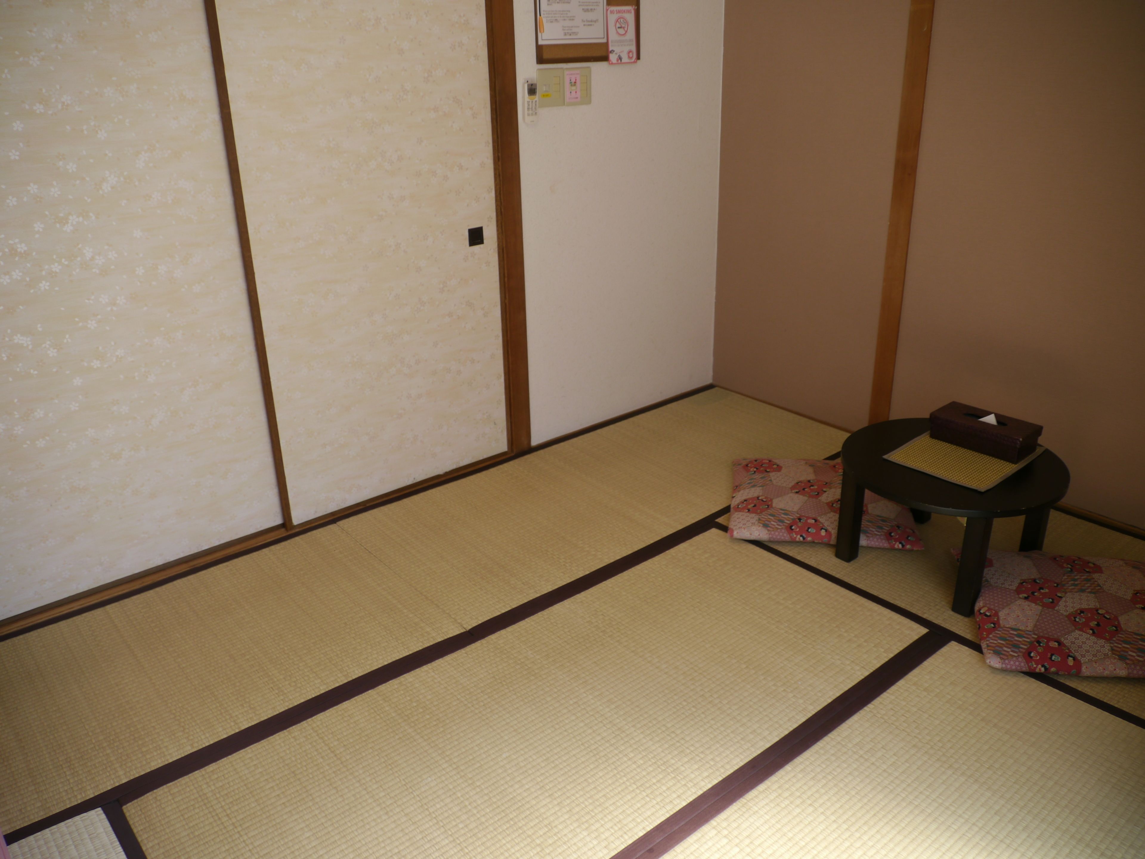 A tatami mat room with a shoji screen door, a small table with a tissue box, and a cushion.