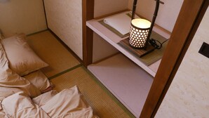 Une pièce de style japonais traditionnel, avec un sol recouvert de tatamis, un futon servant de lit, une étagère ornée d’une lanterne décorative et une petite table avec un tapis.