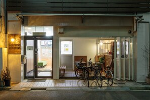 Entrada de restaurante com porta de vidro, uma bicicleta estacionada e um banco de madeira no interior.