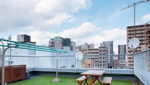 Une terrasse sur le toit, avec un revêtement de gazon synthétique, une table en bois et une rambarde en métal.