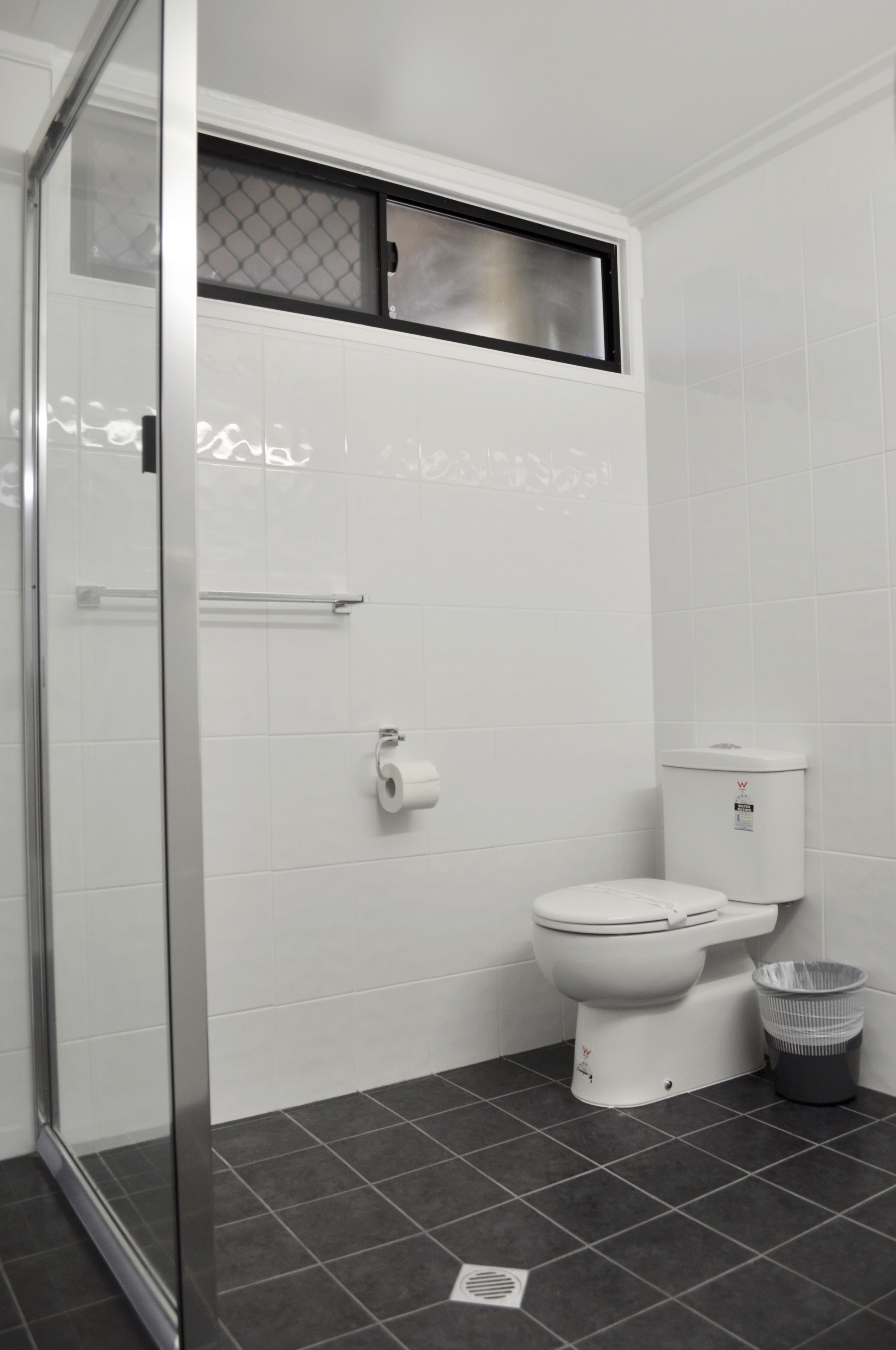 Bagno con box doccia in vetro, un water e un cestino.