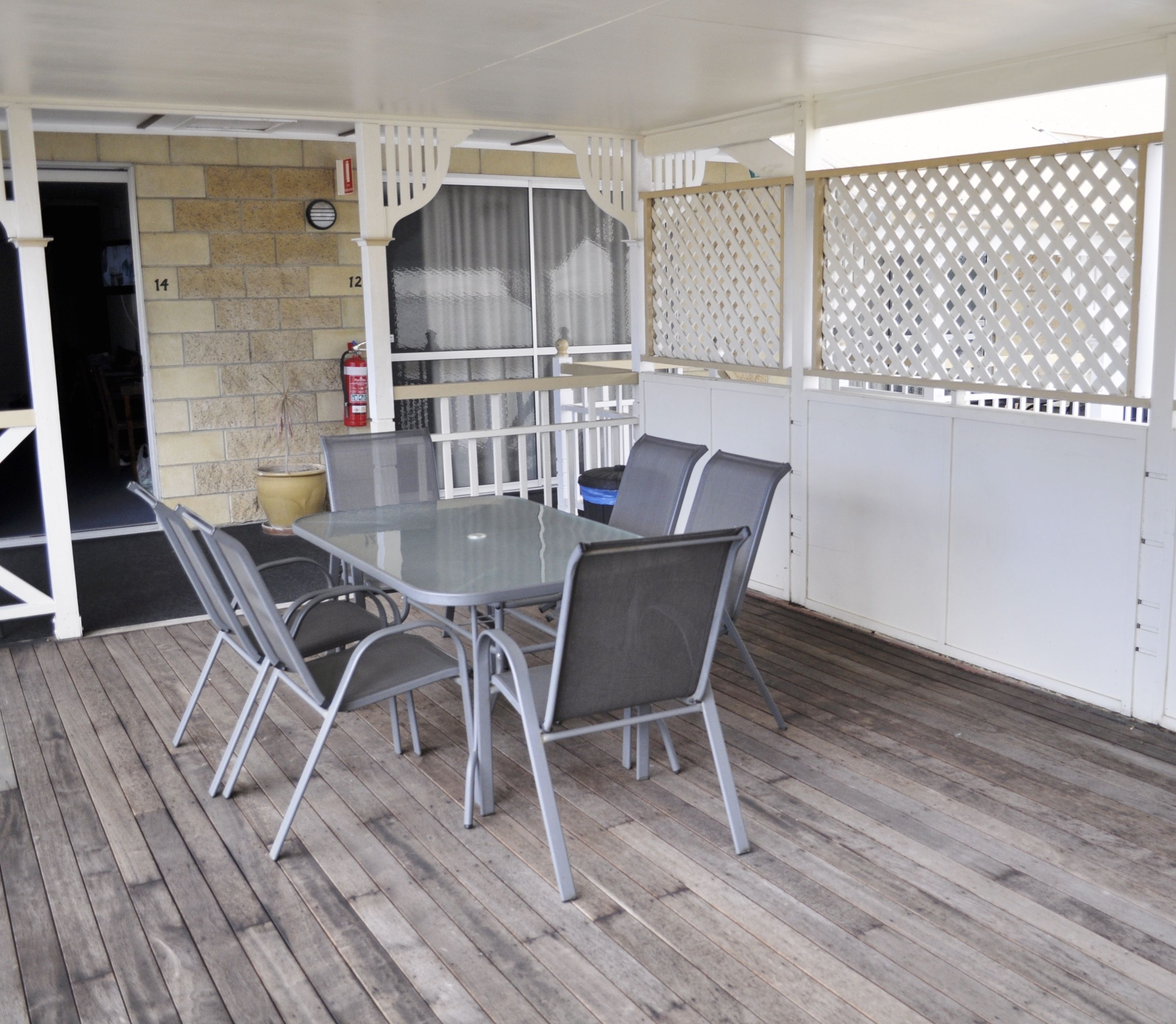 Un patio al aire libre con una mesa y sillas, un extintor y vistas a través de una celosía.