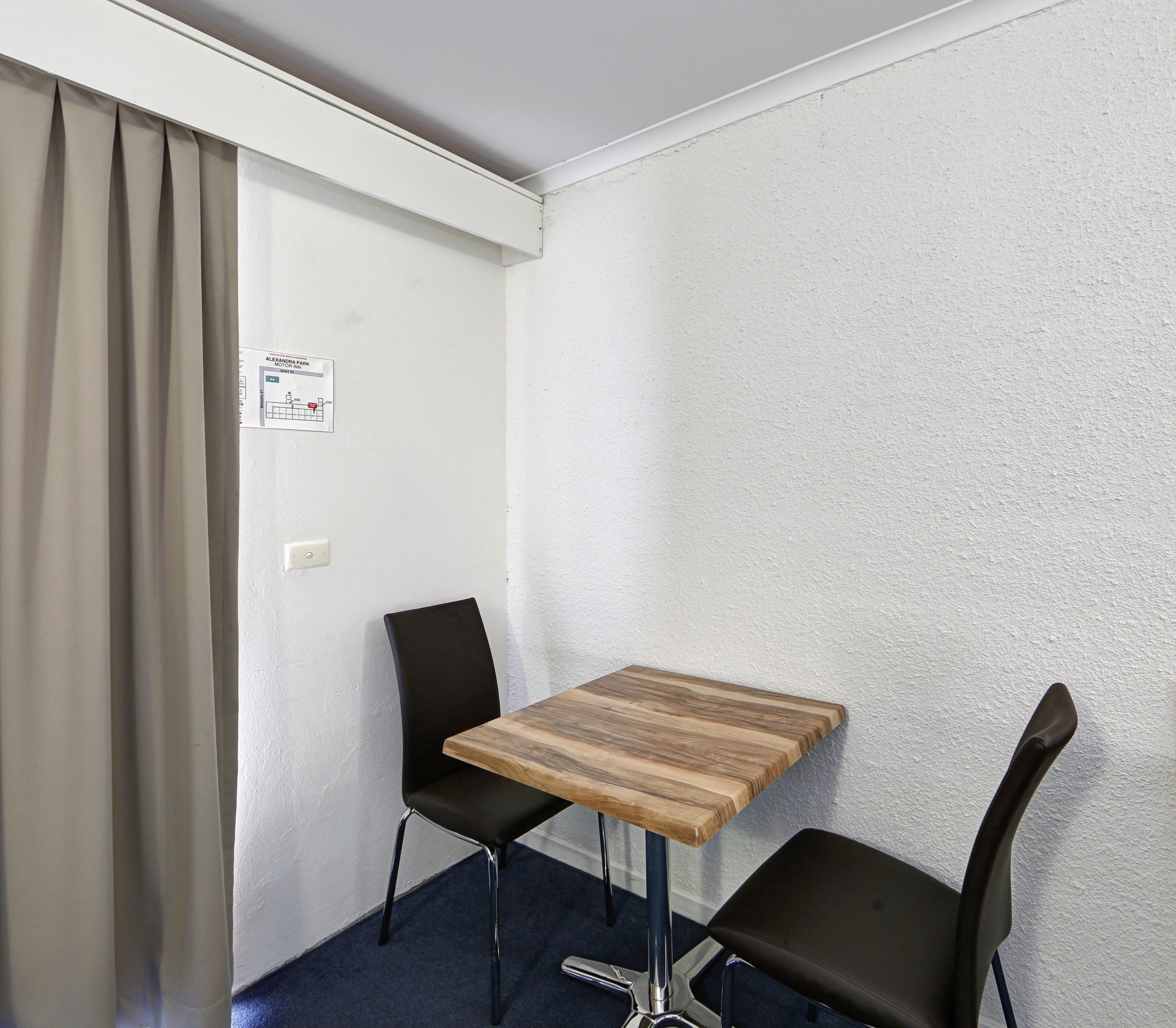 A small room with a wooden table and two black chairs, a white wall with a map, and a curtain.