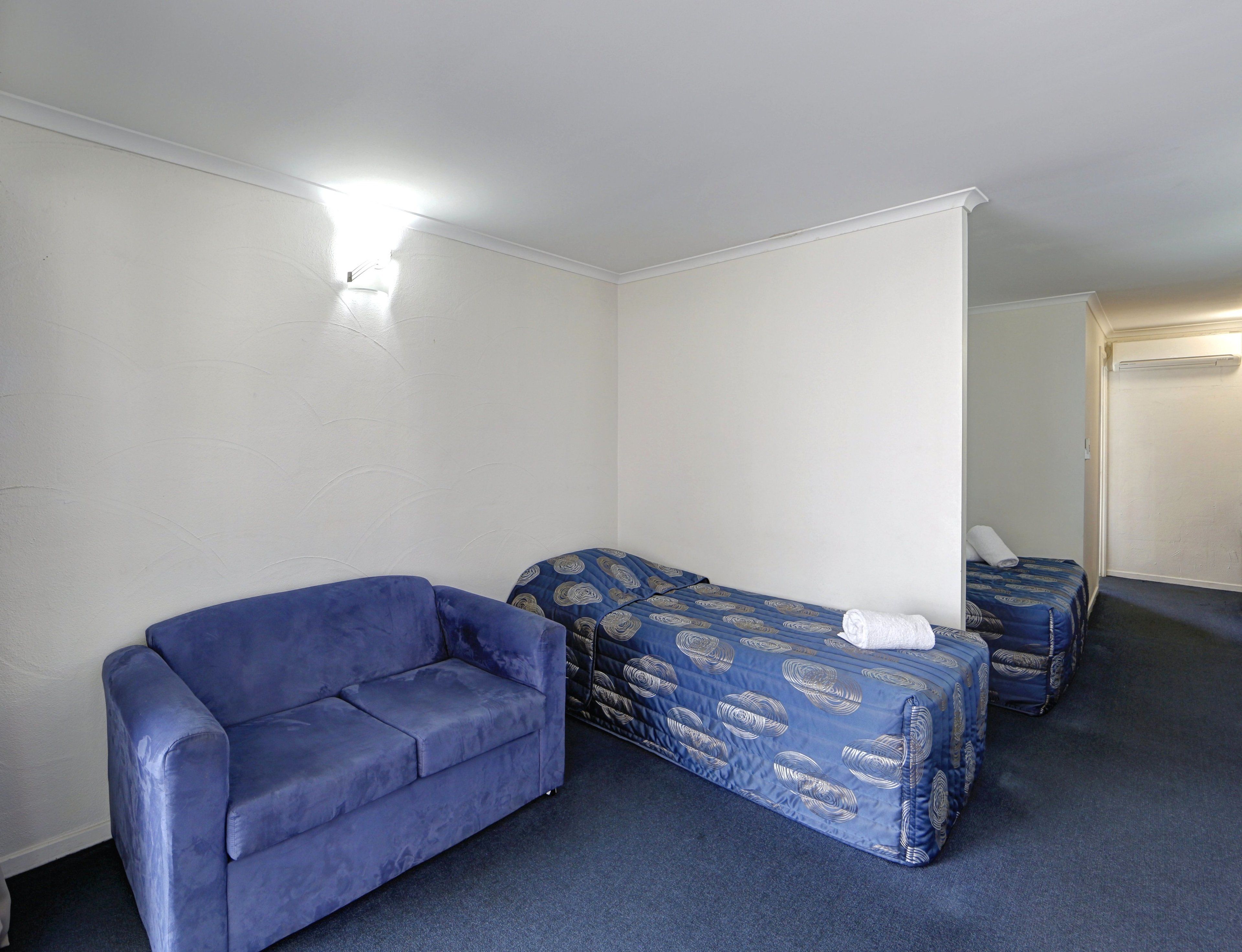 A room with a blue sofa, a bed with a patterned duvet, and a small table.