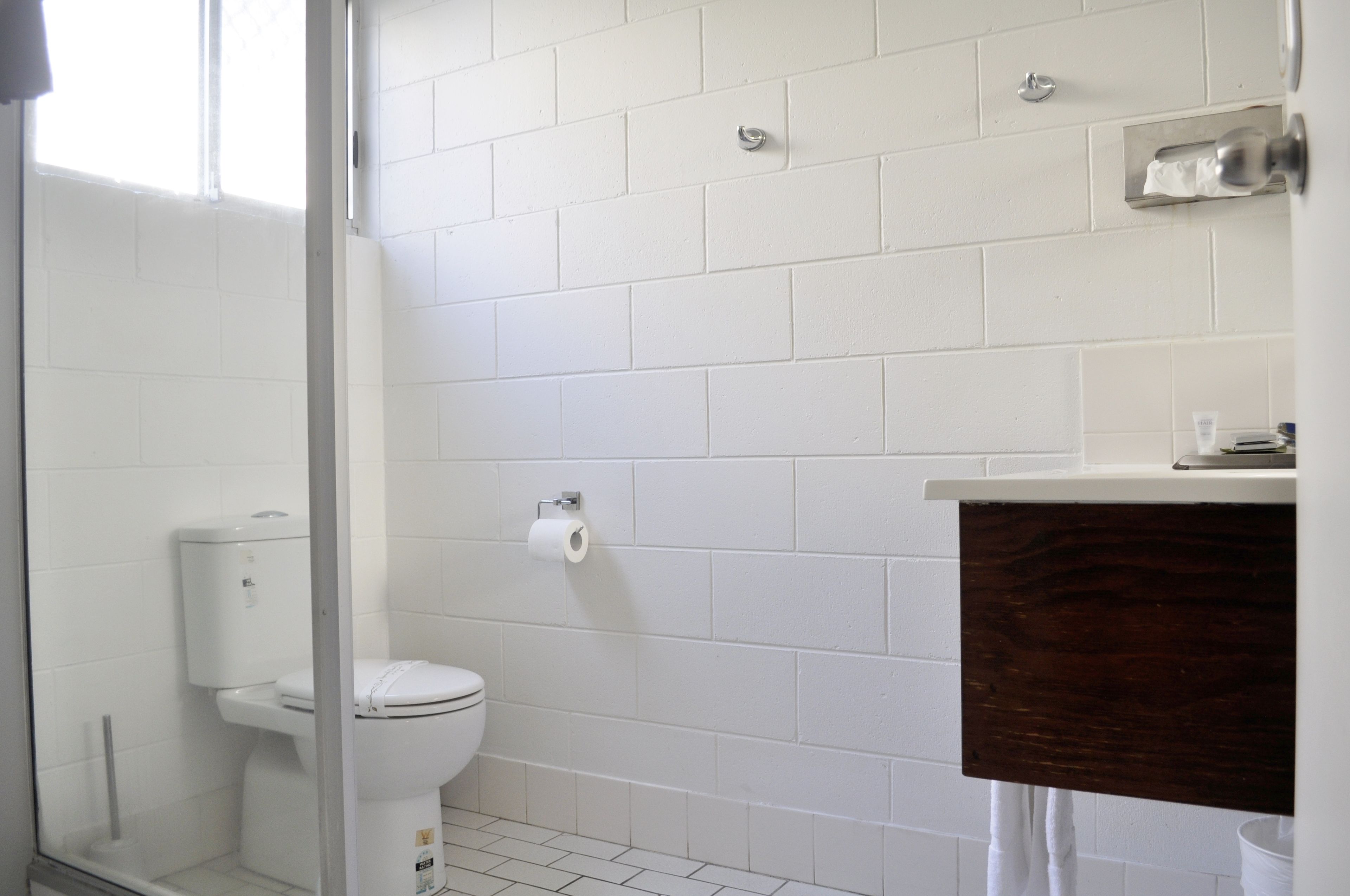 A bathroom with white tiles, a toilet, a paper towel dispenser, and a wooden vanity.