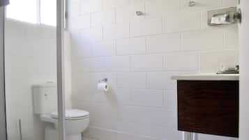 A bathroom with white tiles, a toilet, a paper towel dispenser, and a wooden vanity.