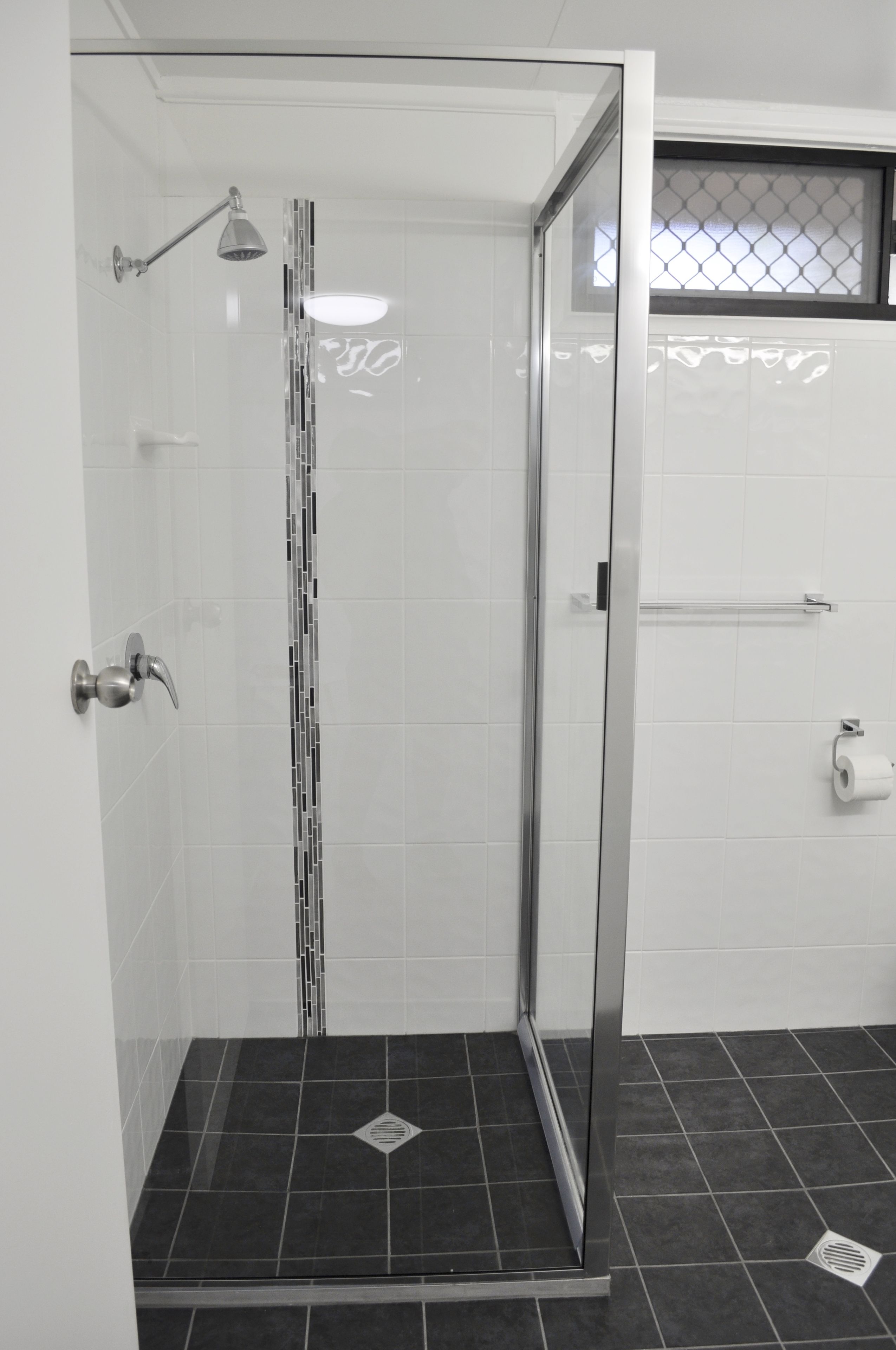 A glass-enclosed shower with a handheld showerhead, a towel rack, and a toilet paper holder on the wall.