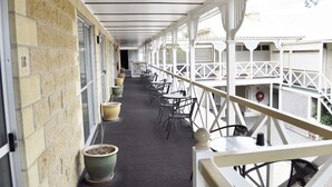 A covered corridor with potted plants, outdoor seating, and a white railing. - Alexandra Park Motor Inn (Bundaberg West)