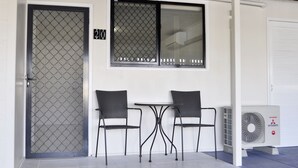 A building entrance with a numbered door, two chairs, a table, and an air conditioning unit. - Alexandra Park Motor Inn (Bundaberg West)