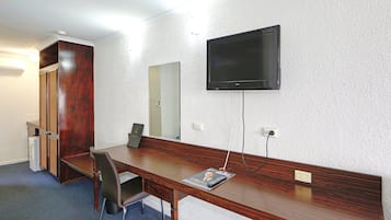 Habitación de hotel con un escritorio de madera, una silla, un televisor en la pared y un espejo.