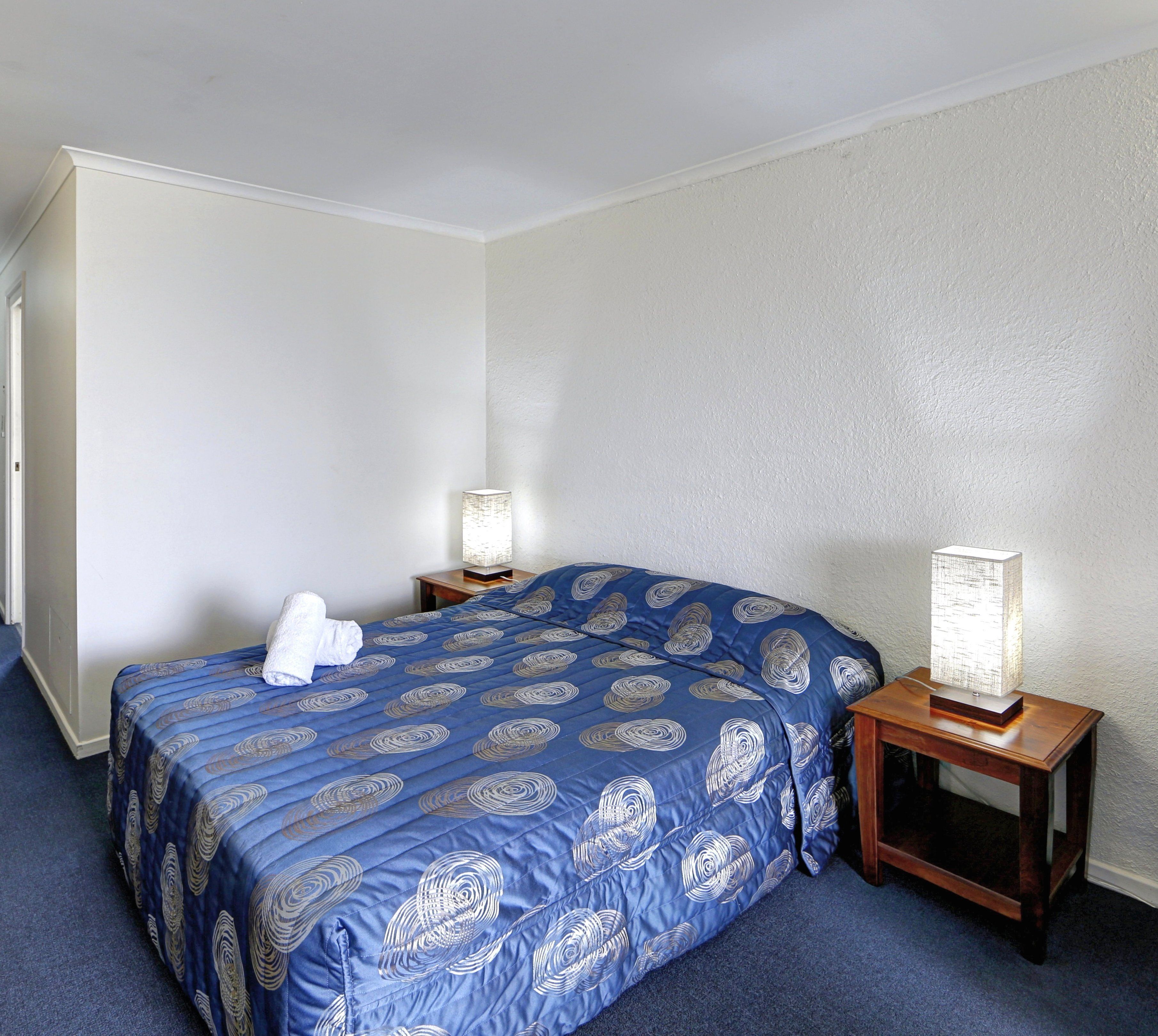A hotel room with a single bed, two bedside tables, and a nightstand with a lamp.
