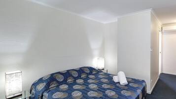 A hotel room with a bed, a bedside table, a lamp, and a window with blinds.